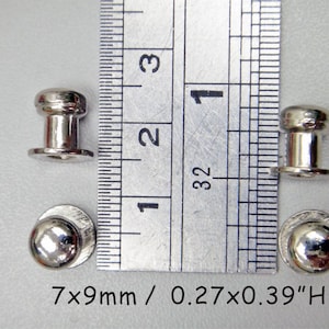 May include: Four silver metal rivets, two with a round head and two with a cylindrical head, measured against a ruler. The rivets are 7mm x 9mm or 0.27 inches x 0.39 inches in height.