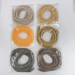 Puede incluir: Seis carretes de ribete de tela de diferentes colores, cada uno envuelto en plástico. Los colores son beige, marrón claro, amarillo, dorado, gris y marrón.