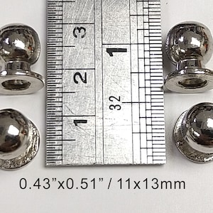Pode incluir: Quatro botões redondos de metal prateado com acabamento liso e brilhante. Cada botão tem uma base redonda com um furo no centro. Os botões medem 0,43" x 0,51" ou 11 x 13 mm.
