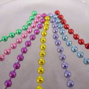 May include: Six strands of metallic chain, each a different color: green, pink, purple, yellow, light blue, and red. The chains are arranged in a fan shape, with the ends of each chain pointing towards the center.