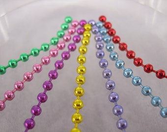 May include: Six strands of metallic chain, each a different colour: green, pink, purple, yellow, light blue, and red. The chains are arranged in a fan shape, with the ends of each chain pointing towards the centre.