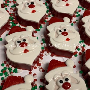 May include: A close-up of several red and white Santa Claus shaped candies with white sprinkles on a white surface. The candies have a white face with black eyes, a red nose, and a white beard. The text "HOW SWEET IT IS BY MELISSA" is visible on the surface.