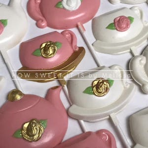 May include: Assortment of pink and white chocolate lollipops shaped like teacups and teapots. Each lollipop features a gold accent and a small white rose. The text "HOW SWEET IT IS by Melissa" is visible at the bottom of the image.