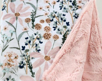 May include: A soft pink and white baby blanket with a floral print. One side of the blanket is made of a soft, plush fabric, while the other side is made of a cotton fabric with a floral pattern.