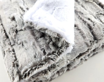 May include: A soft, grey and white faux fur throw blanket with a fluffy texture. The blanket is folded in half and the white side is facing up.