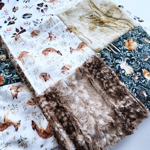 May include: A patchwork baby blanket featuring woodland animal prints. The blanket combines various fabrics, including a soft, faux fur trim and panels with deer, foxes, and paw prints. The color palette includes white, brown, and forest green.