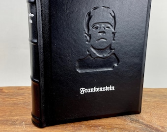 May include: A black leather-bound book with the title "Frankenstein" embossed on the cover. The author, Mary Shelley, is also embossed on the cover. The book features a raised image of the monster from the novel.