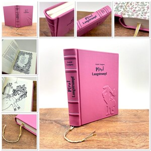 Puede incluir: Un libro de tapa dura rosa titulado "Pippi Langstrumpf" de Astrid Lindgren. La portada presenta una ilustraci&oacute;n en relieve de Pippi y el lomo tiene el t&iacute;tulo verticalmente. Una cinta dorada de marcador se extiende desde el libro.