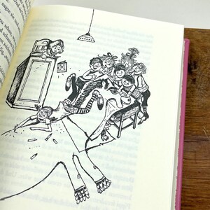 Puede incluir: Ilustraci&oacute;n en blanco y negro de un libro, que representa una escena animada con ni&ntilde;os y una figura grande. La obra presenta l&iacute;neas detalladas, con ni&ntilde;os interactuando alrededor de una mesa y una figura extendida por la p&aacute;gina.