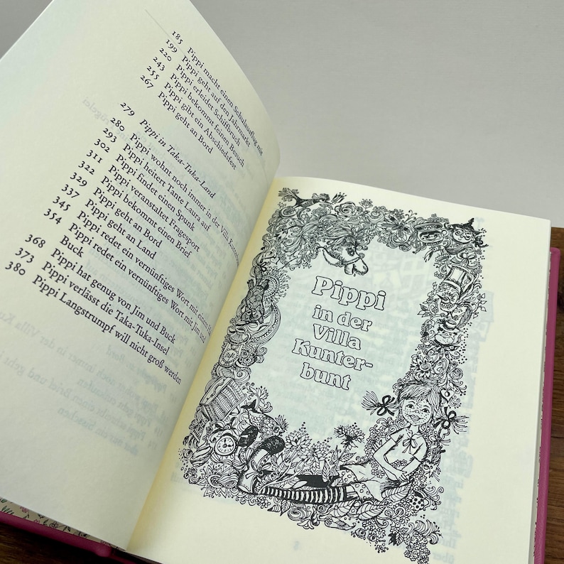 Puede incluir: Un libro abierto con el t&iacute;tulo "Pippi in der Villa Kunterbunt" en un marco decorativo. La p&aacute;gina presenta ilustraciones y texto en blanco y negro, con una cubierta rosa visible en el lado derecho. El libro est&aacute; en alem&aacute;n.
