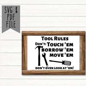 May include: A framed sign with the text "Tool Rules" and the phrases "Don't: Touch 'em, Borrow 'em, Move 'em, Don't even look at 'em!" in black. The frame is brown, and the background is white.
