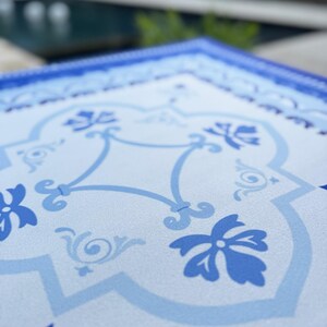 May include: Close-up of a square, light blue and white decorative tray with a floral and scrollwork pattern. The tray has a dark blue border and a repeating design of stylized flowers and vines.