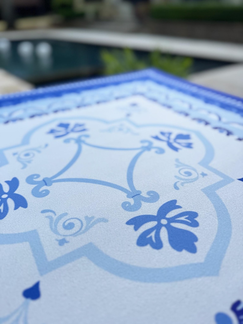 May include: Close-up of a square, light blue and white decorative tray with a floral and scrollwork pattern. The tray has a dark blue border and a repeating design of stylized flowers and vines.