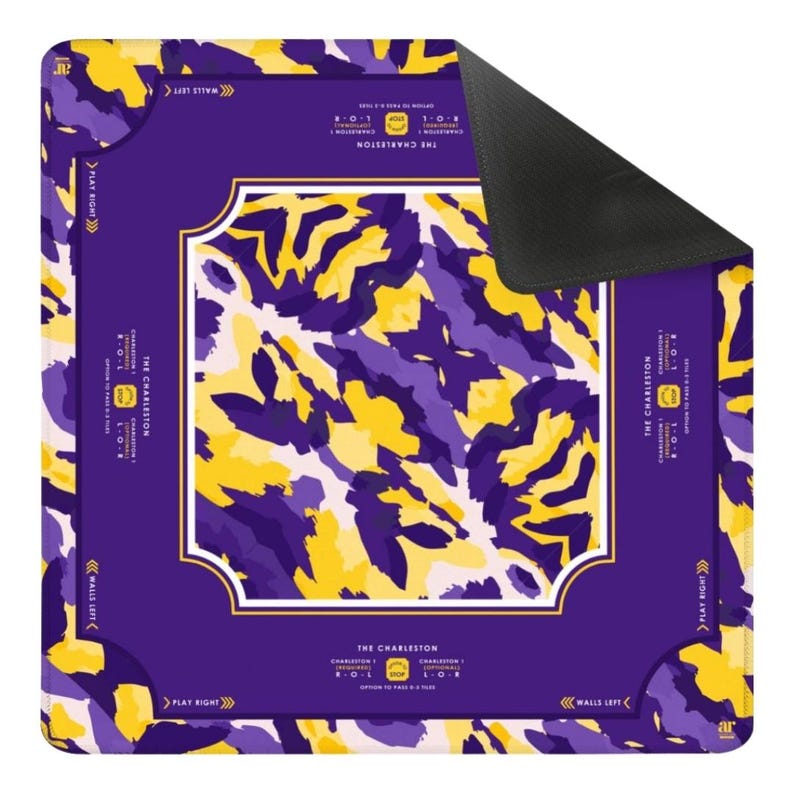 May include: A square game mat featuring a purple and yellow abstract camouflage pattern. The center is framed by a solid purple border with white text reading THE CHARLESTON, PLAY RIGHT, and WALLS LEFT. The underside of the mat is solid black.