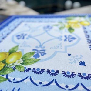 K&ouml;nnte beinhalten: Ein rechteckiger Tischset mit einem wei&szlig;en und blauen Blumendesign. Das Tischset zeigt ein Muster aus Zitronen, Bl&auml;ttern und Blumen. Der Rand ist tiefblau mit einem gewellten Rand.