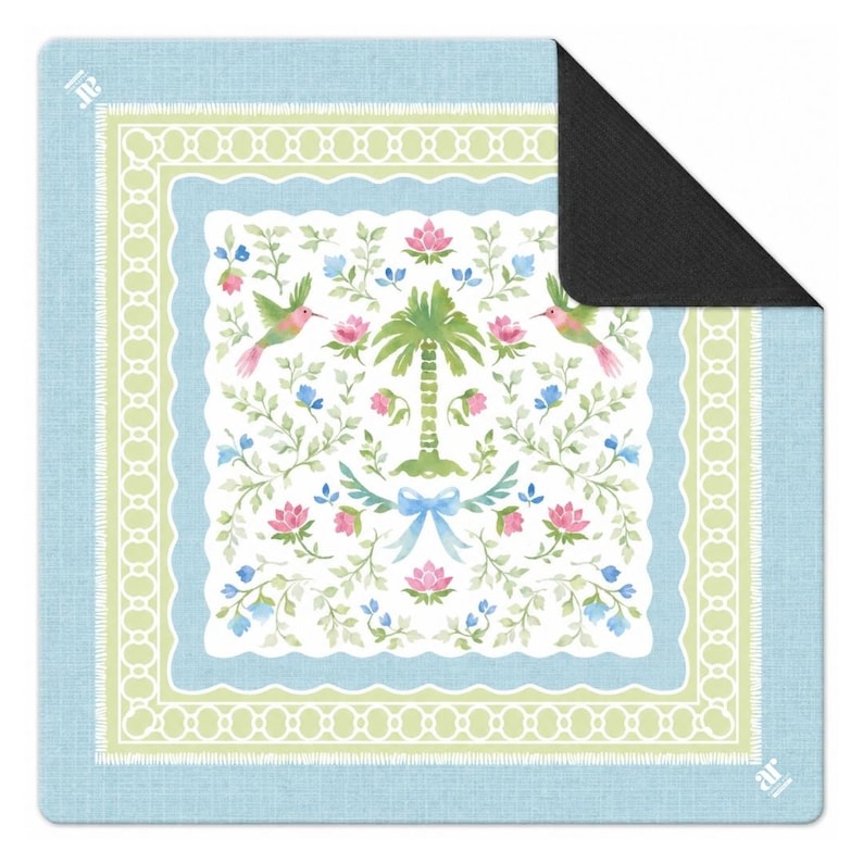 May include: A square doormat with a light blue border and a central design featuring a palm tree, pink flowers, and hummingbirds. The design is framed by a scalloped edge and a white decorative border. The doormat has a black backing.