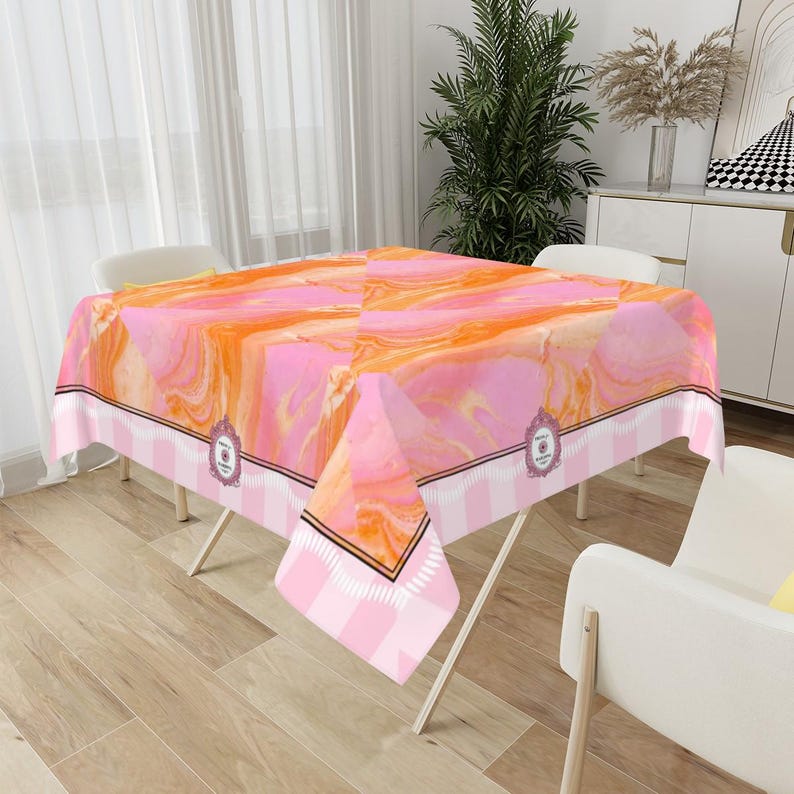 May include: A rectangular tablecloth with a pink and orange marble design. The tablecloth has a white and pink striped border with a decorative emblem. The tablecloth is set on a folding table.