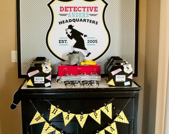May include: A black table with a yellow and white banner that says "Happy Birthday". There are party favors in boxes that say "Detective" and a sign that says "Detective -Anders- Headquarters Est. 2005".