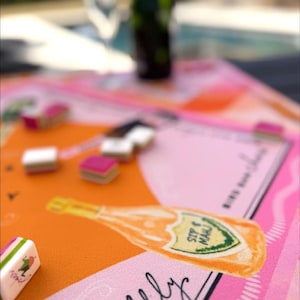 May include: A colorful table setting with a pink, orange, and white design. The table features a champagne bottle illustration with the words "SIP & MAU" and the word "bubbly". Small, rectangular objects with pink and white accents are scattered across the table.