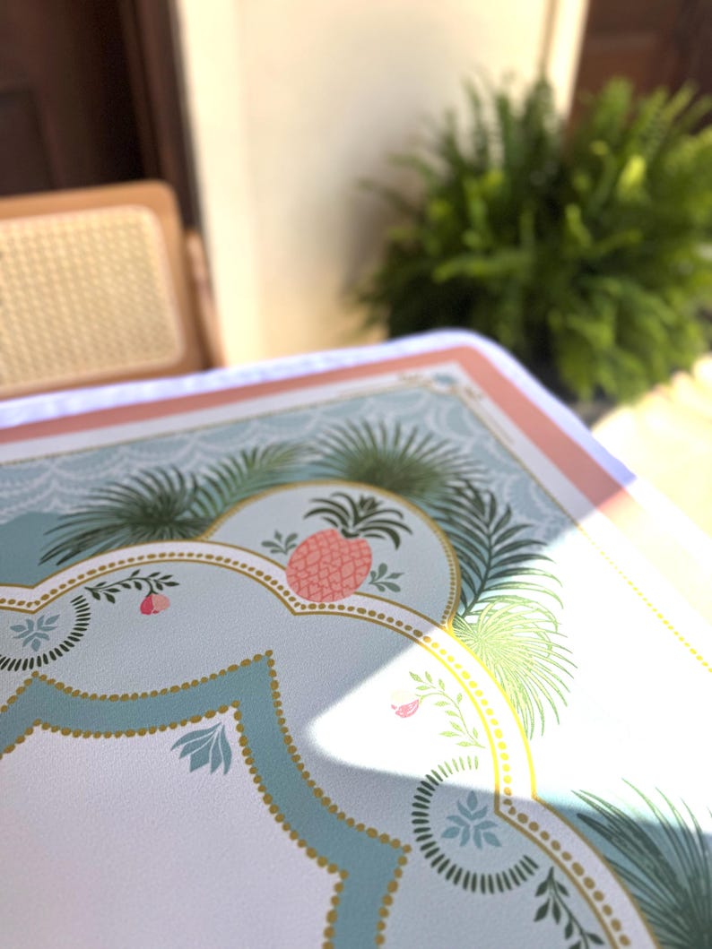 May include: A decorative serving tray with a light blue background and a pink and gold border. The tray features a pink pineapple design and green palm fronds. The tray is likely used for serving food or drinks.