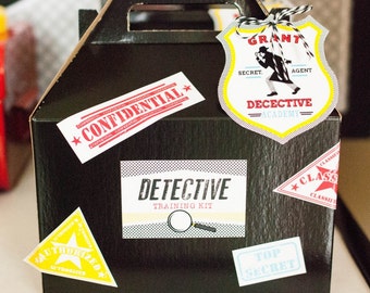 May include: A black cardboard box with a handle, decorated with colorful stickers. The stickers say "Confidential", "Detective Training Kit", "Grant Secret Agent Detective Academy", "Authorized", "Top Secret", and "Classified".