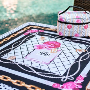 Op de afbeelding: Een decoratieve picknickdeken en bijpassende cosmetische tas. De deken heeft een zwart-wit ontwerp met gouden kettingaccenten, roze rozen en een parfumflesje. De cosmetische tas heeft een vergelijkbaar bloemenpatroon.