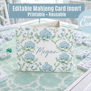 Könnte beinhalten: Ein personalisierter Mahjong-Karteneinsatz mit einem Blumendesign mit blauen Hortensien. Der Einsatz ist von Mahjong-Steinen und Würfeln auf einem gemusterten Tisch umgeben. Auf dem Einsatz steht "Megan". Oben im Bild steht "Editable Mahjong Card Insert Printable Reusable".
