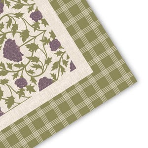 May include: A textile piece featuring a central panel with a cream background, decorated with a repeating pattern of purple flowers and olive green leaves. This central section is framed by a border of olive green fabric with a white plaid pattern.