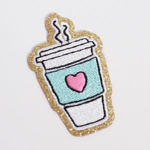 May include: Embroidered patch of a coffee cup with a pink heart on a teal background. The cup has a white lid and steam rising from the top. The patch is outlined in gold glitter.