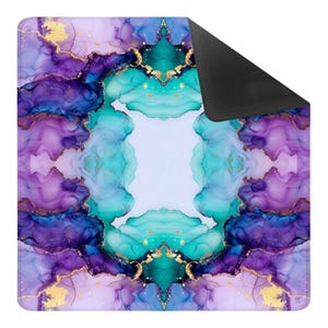 May include: A square desk mat featuring a symmetrical alcohol ink pattern in shades of deep purple, vibrant teal, and light lavender. The design includes intricate gold-colored veining throughout the fluid swirls and a solid black underside.