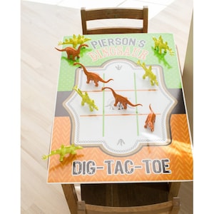 May include: A green and orange dinosaur themed dig-tac-toe game board with plastic dinosaur game pieces. The board says "Pierson's Dinosaur Dig-Tac-Toe".