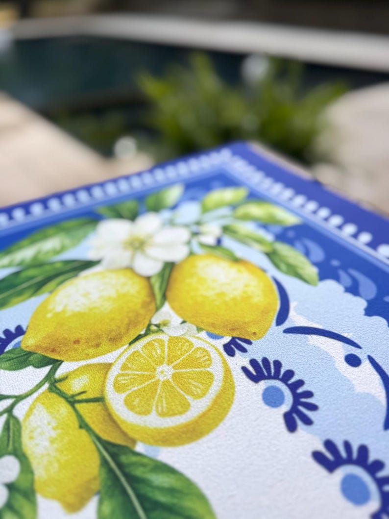 K&ouml;nnte beinhalten: Ein quadratisches dekoratives Tablett mit Zitronenmuster. Das Tablett hat einen blauen Rand mit einem wei&szlig;en und blauen Blumenmuster. Die Mitte des Tabletts zeigt gelbe Zitronen, wei&szlig;e Bl&uuml;ten und gr&uuml;ne Bl&auml;tter.