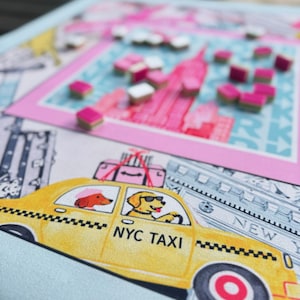 May include: A colorful board game featuring a New York City theme. The game board has a pink and blue cityscape design with small, pink and white game pieces. A yellow NYC taxi with dog passengers is also featured.