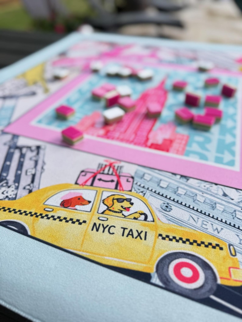 May include: A colorful board game featuring a New York City theme. The game board has a pink and blue cityscape design with small, pink and white game pieces. A yellow NYC taxi with dog passengers is also featured.