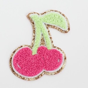 May include: A decorative cherry patch with a textured, pink fruit design and light green stem. The patch is outlined with a gold glitter border, adding a touch of sparkle. This embroidered patch is ideal for adding flair to clothing or accessories.