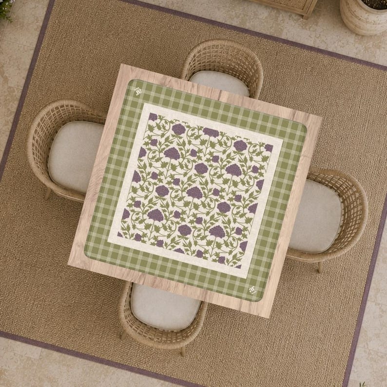 May include: A square table with a light wood finish features a decorative top surface. The center displays a white square with a repeating pattern of purple flowers and green vines, bordered by a wide green and white checkered frame pattern.