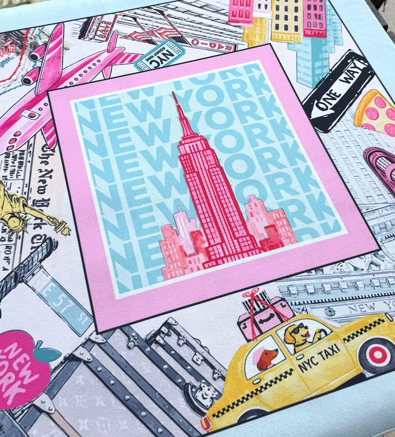 May include: A square scarf with a New York City theme. The design includes the Empire State Building, a yellow taxi with dogs, pink airplanes, and the words "New York" in a repeating pattern. The scarf has a light blue border.