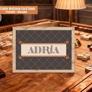 以下が含まれることがあります： マージャンカードカバー。装飾的なフォントで「ADRIA」という名前が書かれています。木製のフレームで、背景は濃い灰色のひし形模様です。木製のテーブルにマージャン牌が置かれています。上部には「Editable Mahjong Card Cover」と書かれています。