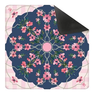 May include: A square floral patterned mat featuring a navy blue center with pink flowers and green leaves arranged in a circular design. The mat has a pink and white checkered border and a black corner.