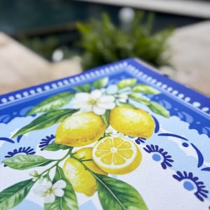 K&ouml;nnte beinhalten: Ein quadratisches, dekoratives Tablett mit Zitronenmuster. Das Tablett zeigt gelbe Zitronen, gr&uuml;ne Bl&auml;tter und wei&szlig;e Bl&uuml;ten vor einem hellblauen und wei&szlig;en Hintergrund. Der Rand ist dunkelblau mit einem floralen Muster.