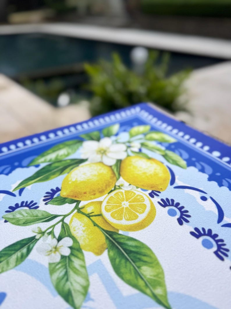 K&ouml;nnte beinhalten: Ein quadratisches, dekoratives Tablett mit Zitronenmuster. Das Tablett zeigt gelbe Zitronen, gr&uuml;ne Bl&auml;tter und wei&szlig;e Bl&uuml;ten vor einem hellblauen und wei&szlig;en Hintergrund. Der Rand ist dunkelblau mit einem floralen Muster.