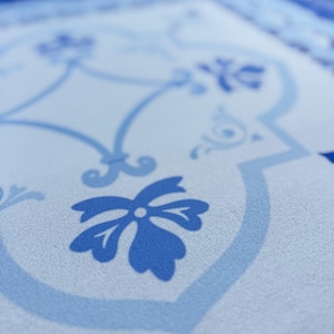 May include: Close-up of a light blue and white patterned surface. The design features floral and geometric elements in varying shades of blue. The pattern is reminiscent of traditional tile work.