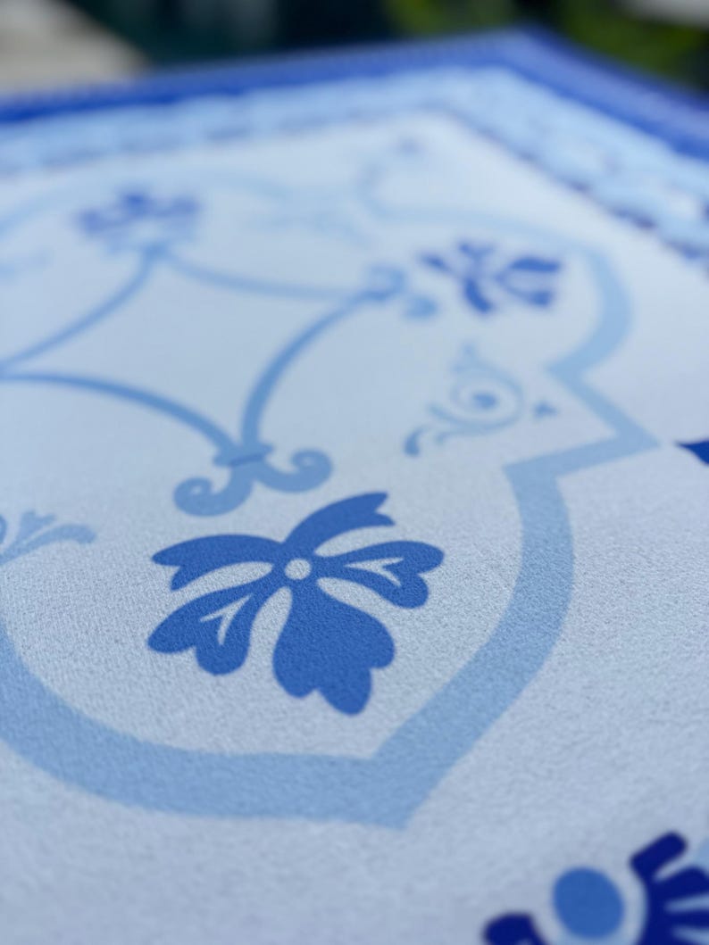 May include: Close-up of a light blue and white patterned surface. The design features floral and geometric elements in varying shades of blue. The pattern is reminiscent of traditional tile work.