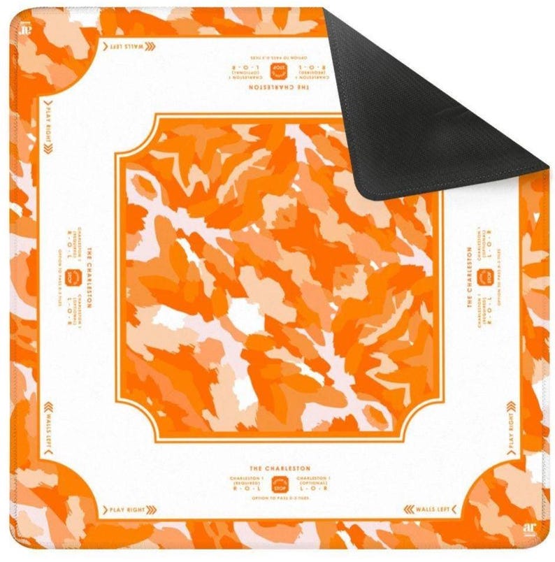 May include: A square game mat featuring a vibrant orange and white camouflage pattern. The white border includes the text THE CHARLESTON, directional arrows labeled PLAY RIGHT and WALLS LEFT, and instructions for passing cards during gameplay.