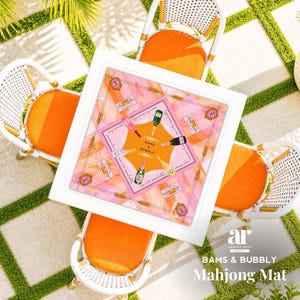 May include: Overhead shot of a white square table with a pink and orange Mahjong mat, surrounded by four white wicker chairs with orange cushions. The mat features champagne bottles and the text "BAMS & BUBBLY".