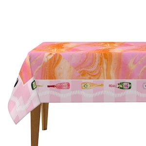 May include: A pink and orange patterned tablecloth with a decorative border featuring champagne bottle illustrations. The table covering has a marble-like design and is draped over a wooden table.