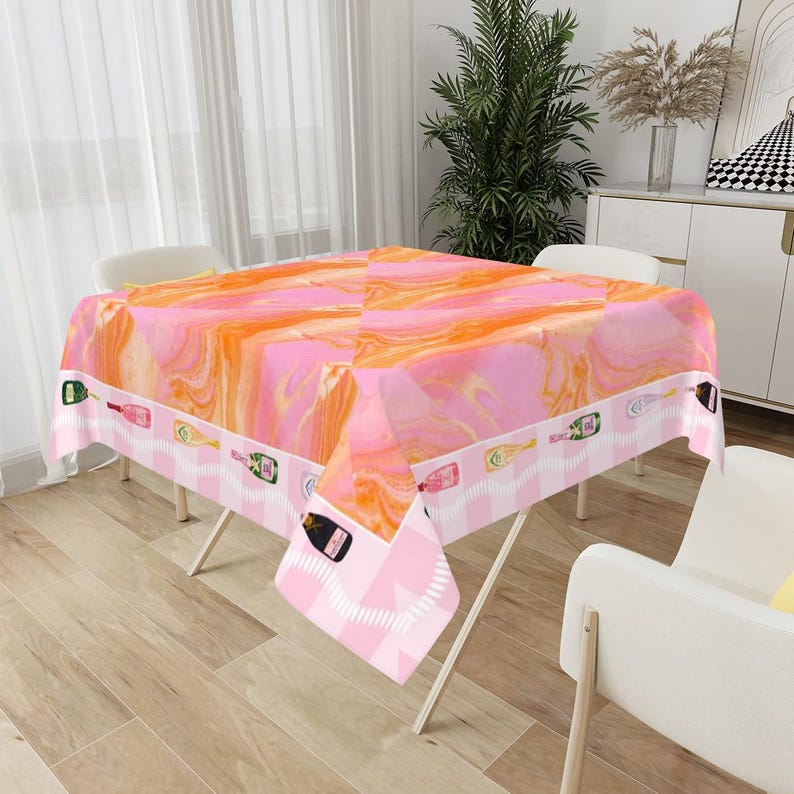 May include: A pink and orange marble-patterned tablecloth with a border featuring champagne bottles. The tablecloth is draped over a table with white chairs. The overall theme is celebratory and festive.