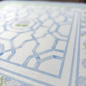 May include: Close-up of a watercolor design featuring a light blue geometric pattern on a white background. The design includes a border and floral accents, creating a decorative and artistic aesthetic.