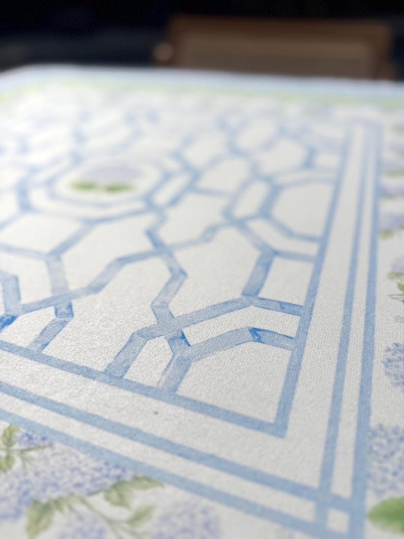 May include: Close-up of a watercolor design featuring a light blue geometric pattern on a white background. The design includes a border and floral accents, creating a decorative and artistic aesthetic.