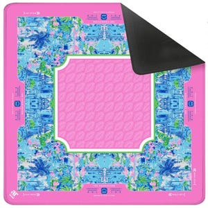 Pode incluir: Um mousepad retangular rosa com um design floral e arquitet&ocirc;nico colorido. O centro apresenta um padr&atilde;o de folhas rosa dentro de uma moldura com bordas brancas. As bordas s&atilde;o adornadas com ilustra&ccedil;&otilde;es florais e de edif&iacute;cios azuis e verdes, com o texto "THE CHARLESTON".
